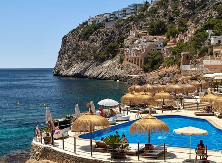 Küstenort mit Pool und Meerblick, felsigen Klippen und Booten.