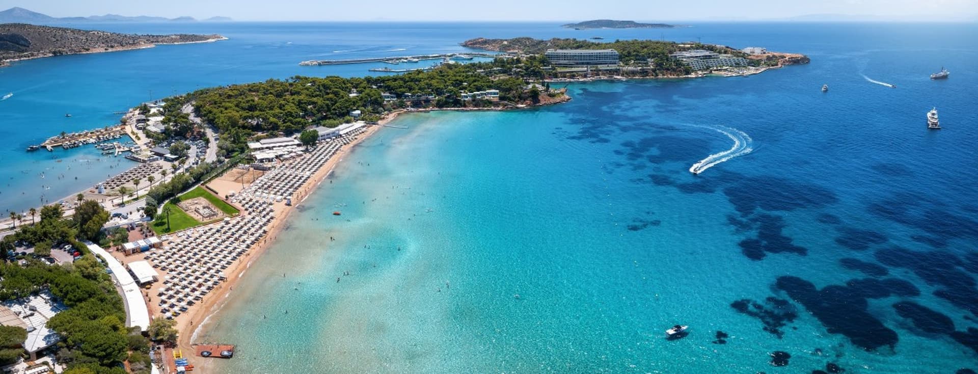 Aerial view of a sandy beach with rows of umbrellas, turquoise water, and boats on a sunny day.