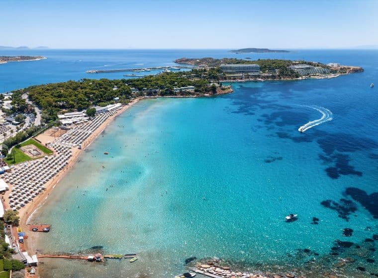 Aerial view of a sandy beach with rows of umbrellas, turquoise water, and boats on a sunny day.
