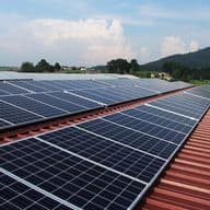 Blick über das Dach einer Gewerbeimmobilie mit Solarpanel in grüner, hügeliger Landschaft