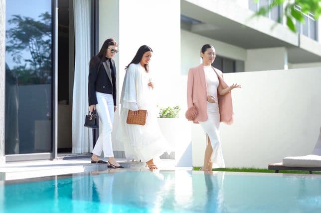 Three women in stylish outfits walking by a poolside, with modern architecture in the background.