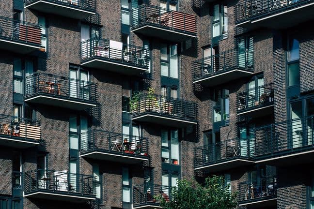 Several modern brick apartment buildings with multiple balconies, some of which have potted plants and outdoor furniture.