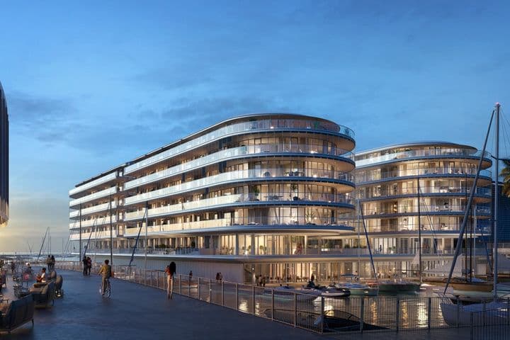 Futuristische Wasserfrontgebäude mit geschwungenen Glasfassaden bei Sonnenuntergang, umgeben von Booten und Palmen, unter einem klaren blauen Himmel.