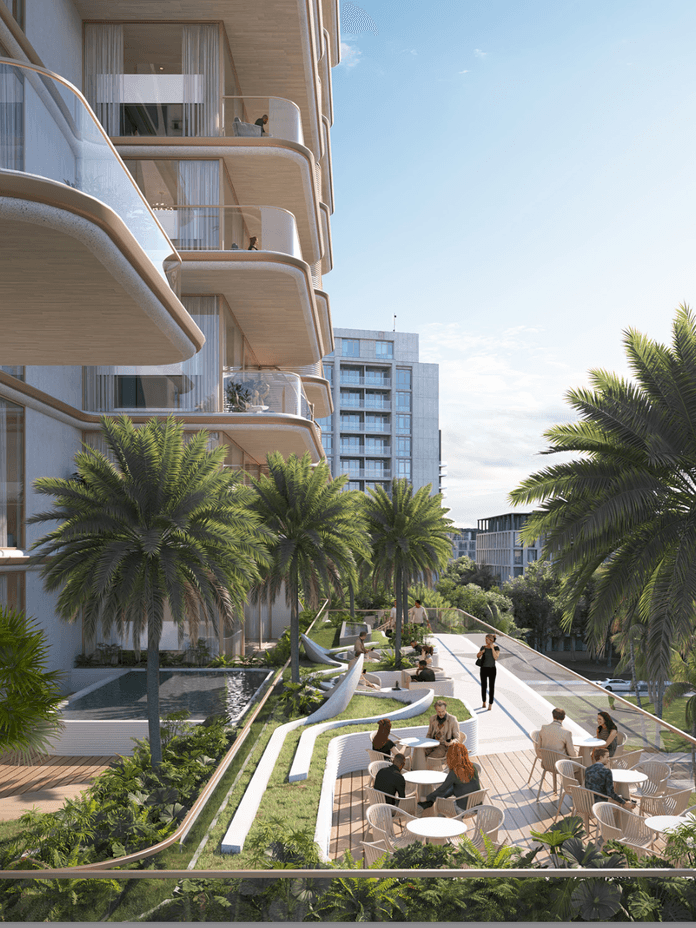 Outdoor terrace at Sunset Bay 5 featuring seating areas, landscaped greenery, palm trees, and views of the building’s balconies and surrounding community.