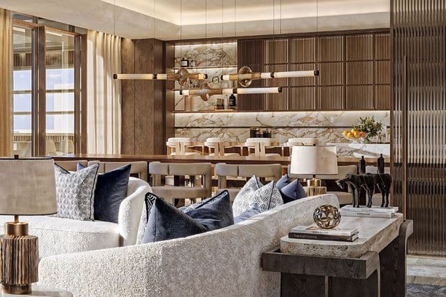 Luxurious living room with a white curved sofa, dark wooden accents, decorative pillows, and a modern chandelier above a marble dining area.