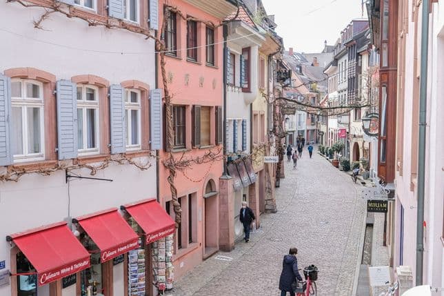 Blick in eine schmale Altstadtgasse in Freiburg mit bunten Fassaden, Ladengeschäften und Passanten