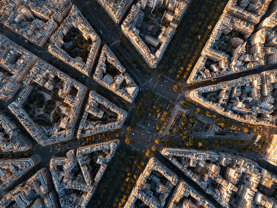 Aerial view of a city's geometric street layout with triangular blocks converging at a central intersection, lined with buildings and trees.
