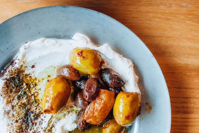 Plate of creamy dip topped with assorted olives and herbs, served with pita bread on a wooden table.
