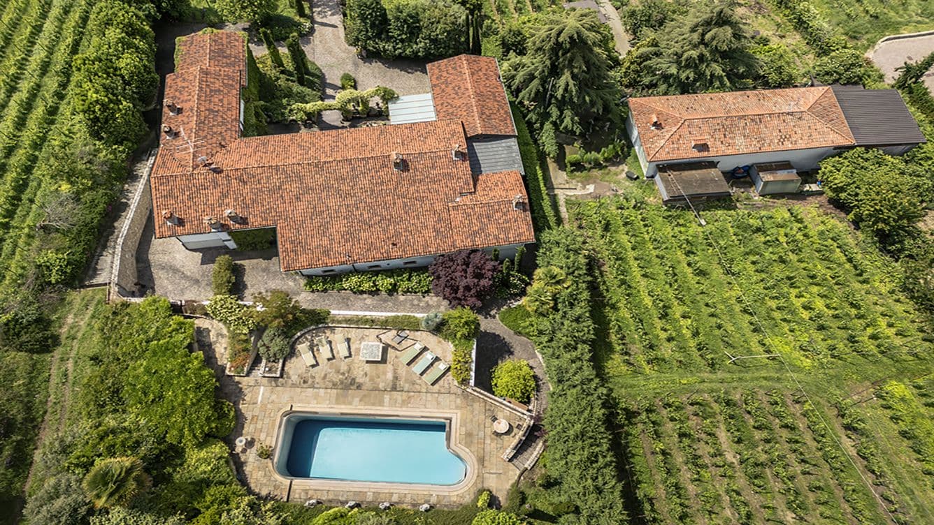 Luftaufnahme eines ländlichen Anwesens mit einem Haus mit rotem Dach, Swimmingpool und umliegenden Gärten und Weinbergen.