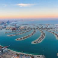 Aerial view of Dubai's Palm Jumeirah, a palm-shaped artificial archipelago, with city skyline and blue sea under a pastel sky.