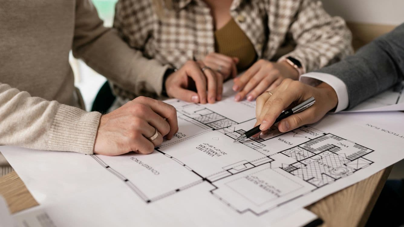 Detall que il·lustra una part del procés de comercialització d’un immoble amb tres persones i el plànol arquitectònic de l’immoble.