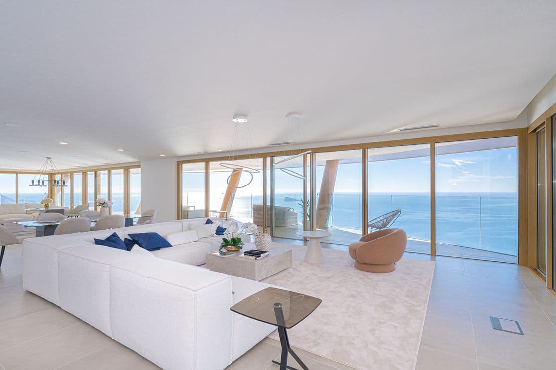 Salon im Penthouse des Intempo-Turms. Weißes Sofa mit blauen Kissen, Esstisch und Panoramaausblick auf das Meer.