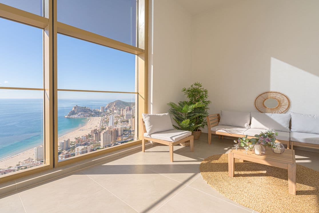 Zimmer mit Meerblick im Intempo-Turm. Rechts sieht man ein Sofa und einen Sessel mit einer Pflanze, und links den Blick auf das Meer und den Strand.