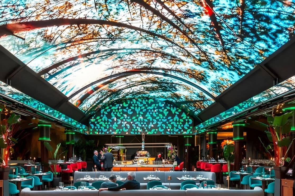 A vibrant restaurant with a vaulted ceiling featuring illuminated tree patterns, modern decor, and diners seated at tables.