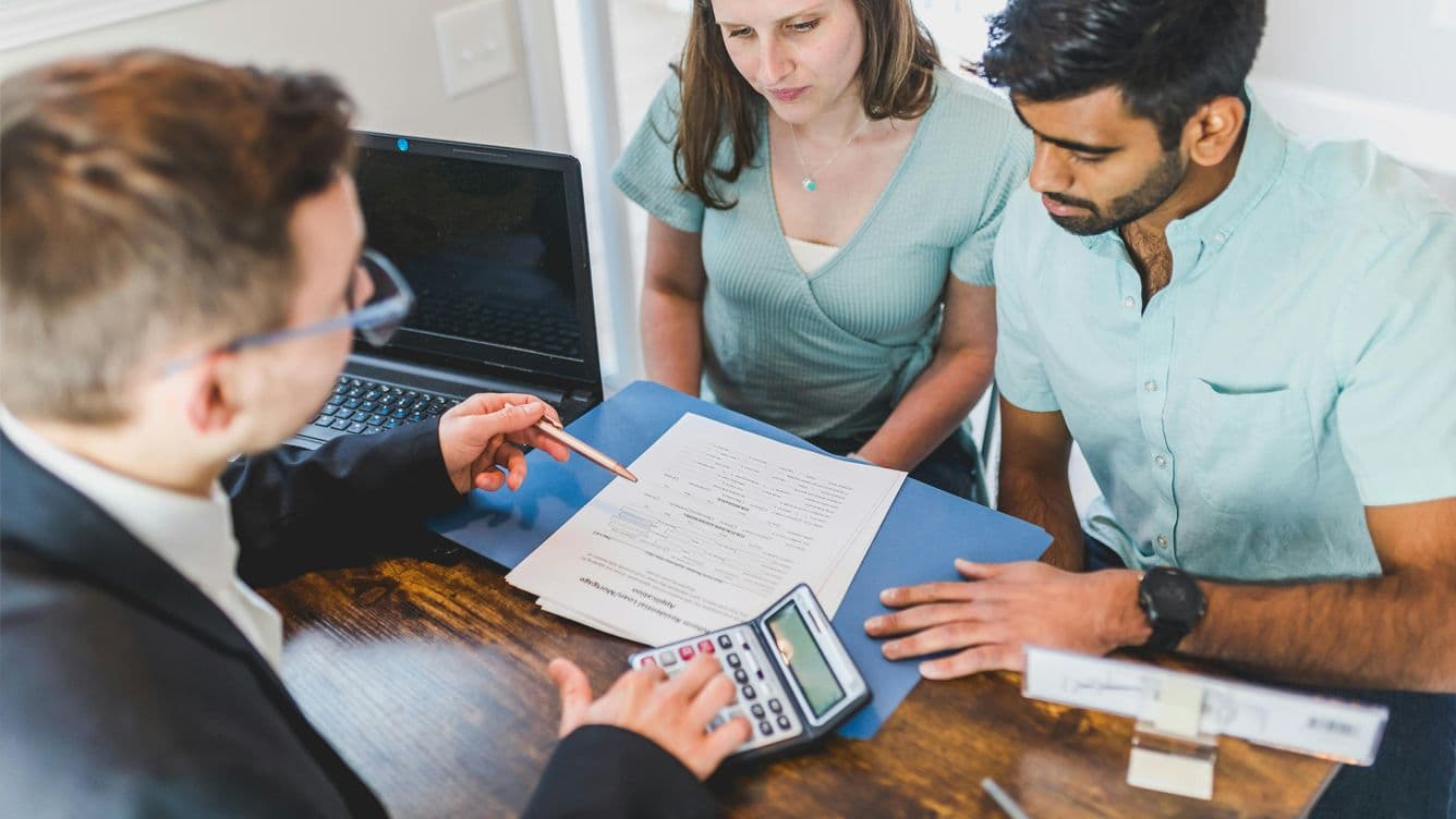 Foto der Unterzeichnung von einer Verkaufsvereinbarung einer Immobilie zwischen einem Immobilienmakler und einem Paar.