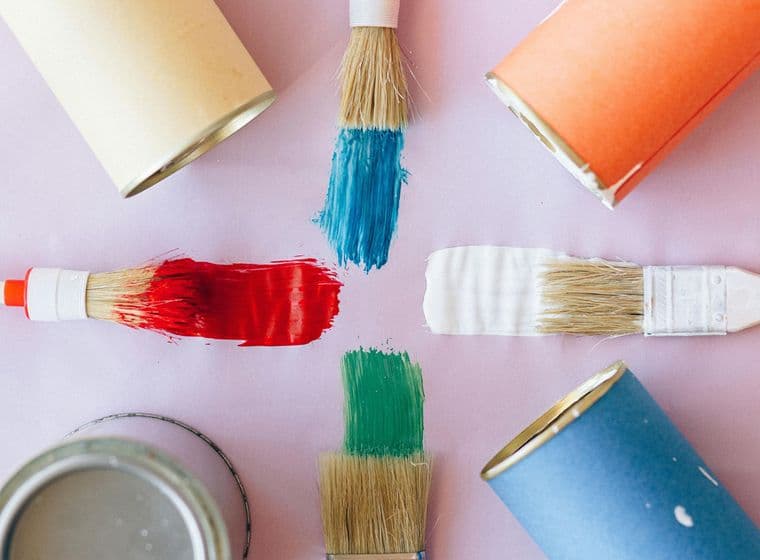 Mostres de pintures sobre una superfície llisa: color blau, taronja, groc i lila. Es veuen 4 pinzells amb colors vermell, blau, blanc i verd.