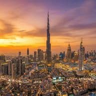 Aerial view of Downtown Dubai at sunset, featuring Burj Khalifa surrounded by illuminated buildings and a winding highway.