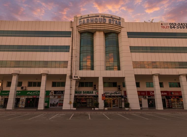 Facade of Garhoud Star building with shops on the ground floor, featuring large columns and glass windows, under a sunset sky.