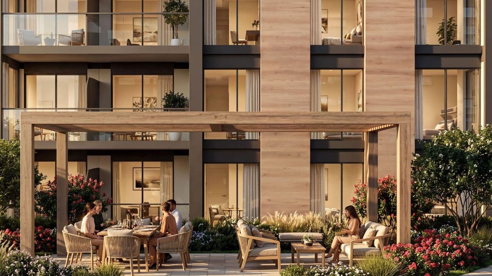 Outdoor terrace with people dining under a wooden pergola, surrounded by greenery and flowers, adjacent to a modern apartment building.