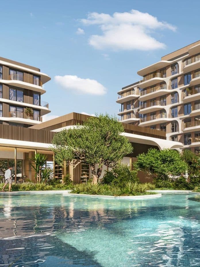 Resort-style swimming pool nestled between low-rise residential buildings, surrounded by landscaped greenery, creating a tranquil wellness-focused environment.