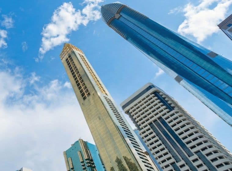Tall modern skyscrapers with reflective glass facades against a bright blue sky with scattered clouds.