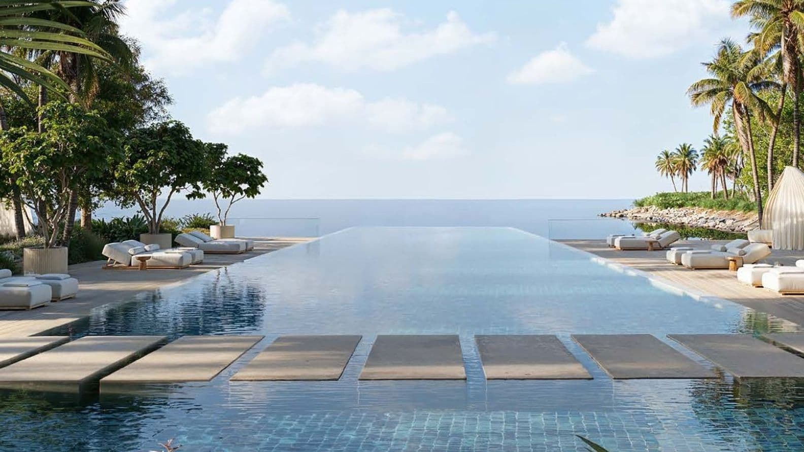 Infinity pool with sunbeds, palm trees, and sea view at Jumeirah Asora Bay.