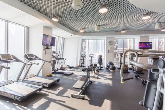Fully equipped fitness center in Cayan Tower Dubai with treadmills, strength machines, and large windows offering panoramic city views.