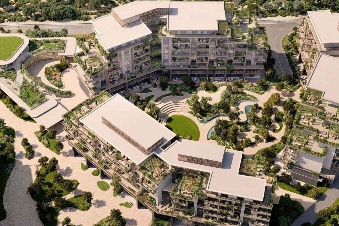 Aerial view of a modern apartment complex with green rooftop terraces, landscaped courtyard, winding pond and pathways.