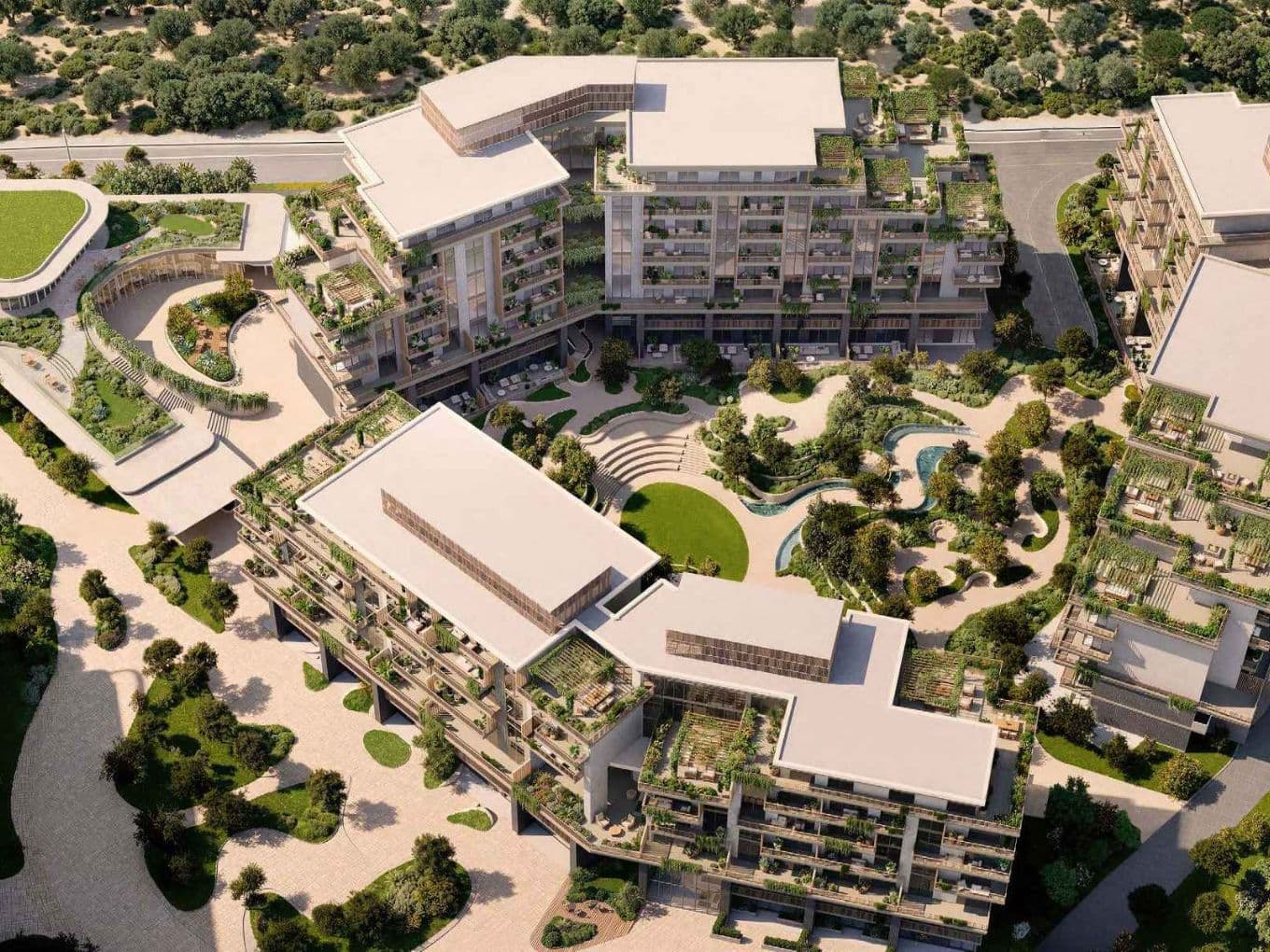 Aerial view of a modern apartment complex with green rooftop terraces, landscaped courtyard, winding pond and pathways.