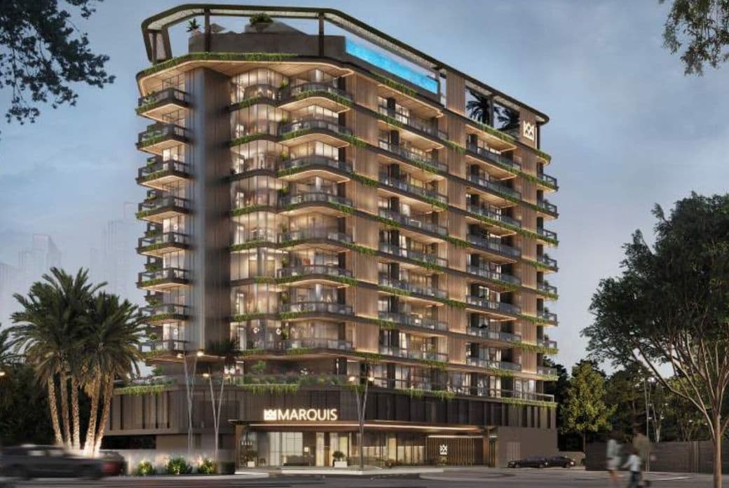 Evening exterior view of Marquis Vista at DLRC by Marquis Development, showcasing the modern glass façade, wraparound balconies, and illuminated architecture surrounded by greenery.