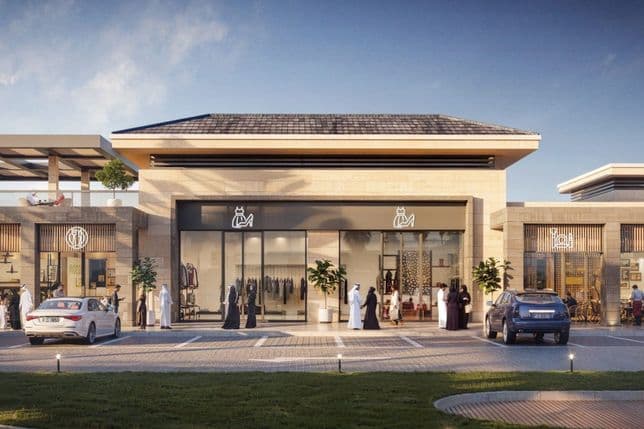 Modern shopping center with large glass windows, parked cars, and people walking. The building features a minimalist design and outdoor seating.