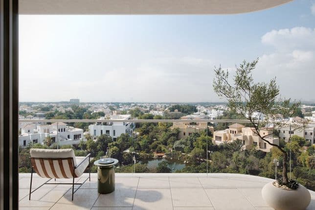 Balcony view of a cityscape with white buildings and greenery, featuring a striped chair, small table, and potted plant in the foreground.