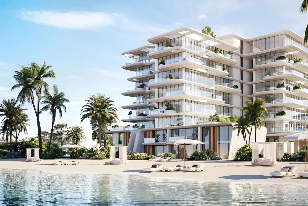 Modern beachfront building with glass balconies, surrounded by palm trees, overlooking a sandy beach and calm sea under a clear blue sky.