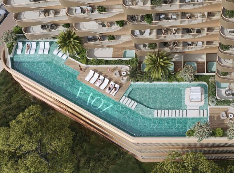Aerial view of a luxurious building with a rooftop pool, sun loungers, and lush greenery, surrounded by curved balconies with outdoor seating.
