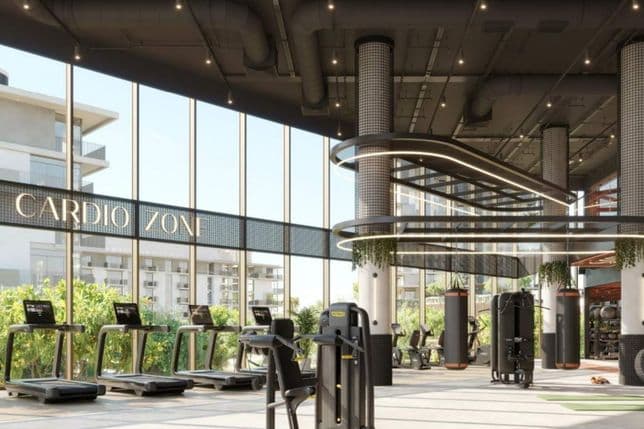 Modern gym with large windows, featuring treadmills, exercise machines, and greenery. Sign reads "Cardio Zone." Bright and spacious interior.