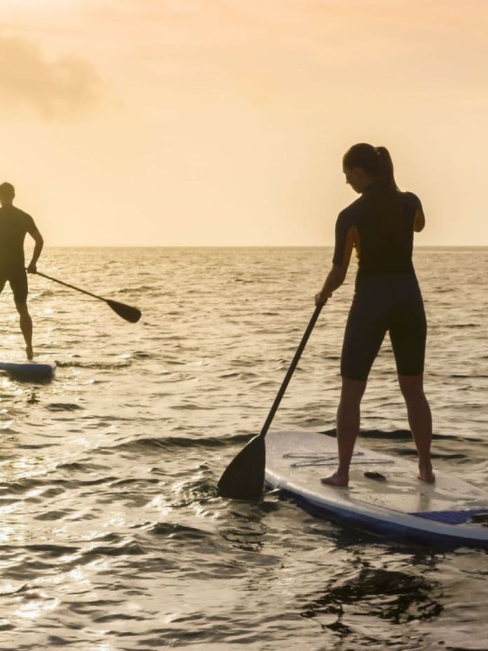 Two people paddleboarding in the sea near Anantara Villas at sunset.