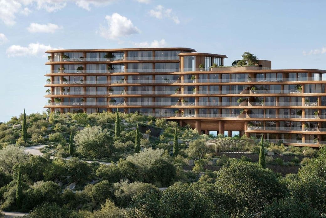 Curved architectural building surrounded by greenery with sea views in the background.