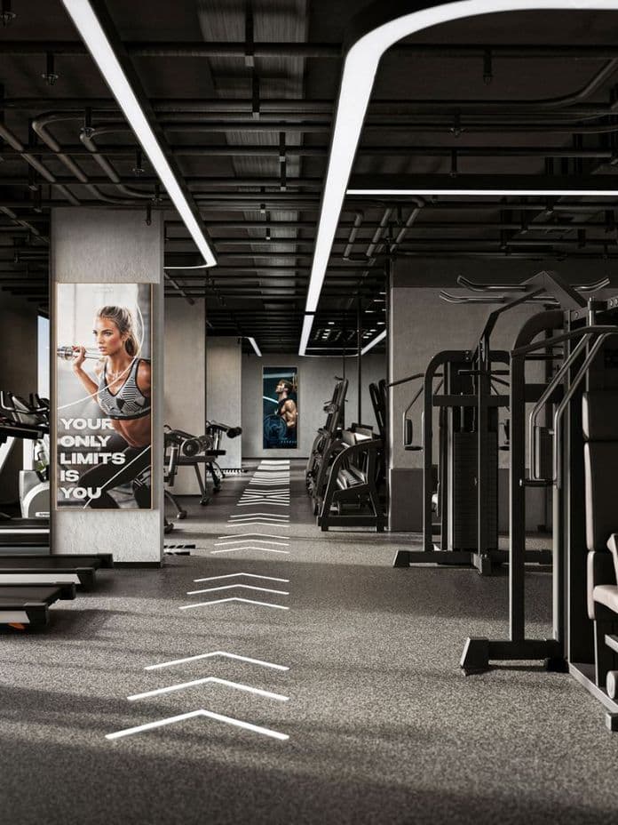 Modern gym interior with treadmills, weight machines, and motivational posters. Large windows allow natural light to illuminate the space.