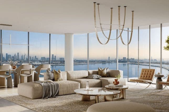 Spacious modern living room with beige sofas, large windows offering city and water views, elegant chandelier, and a round coffee table.