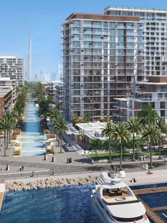 View of Mina Rashid waterfront with luxury yachts docked in the foreground, palm-lined promenades, modern mid-rise residential buildings, and a central water feature leading toward the Burj Khalifa visible in the distant skyline.          Ask ChatGPT