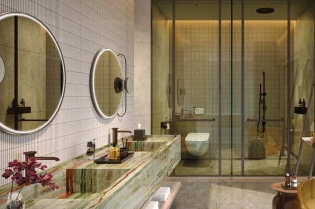 Modern bathroom with a green marble sink, round mirrors, glass shower doors, and warm lighting. Decor includes a vase of purple flowers.
