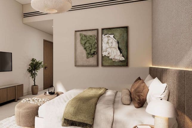 Modern neutral-toned bedroom with upholstered bed, green throw, abstract wall art, pendant light, bedside lamp and potted plant.