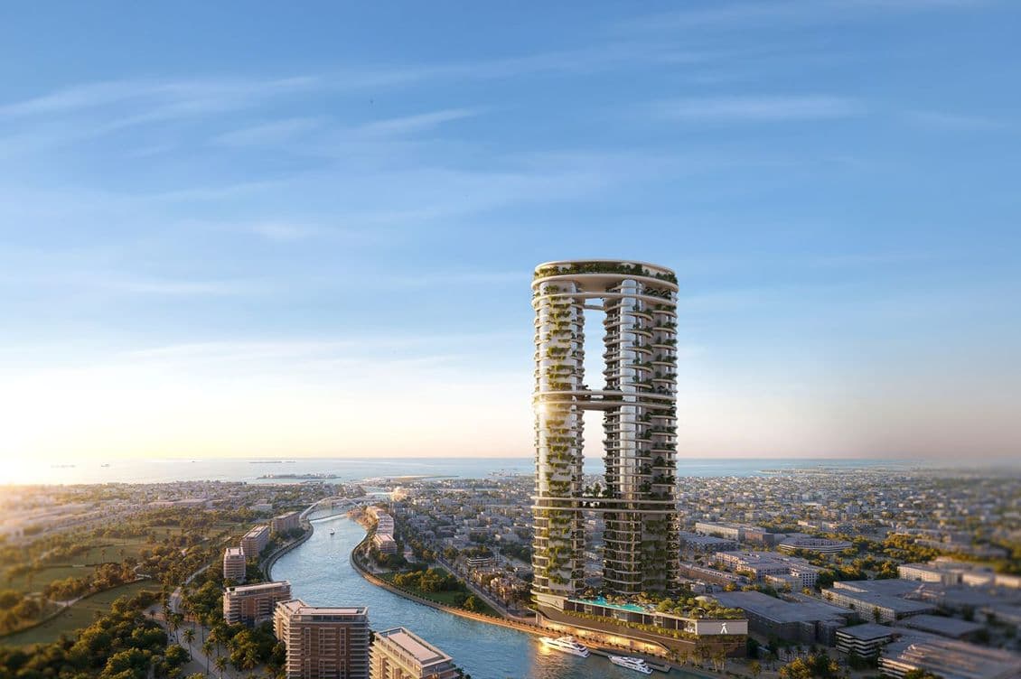 Two circular towers linked by a sky bridge, covered in greenery, rising beside a winding canal with boats and a distant city under a blue sky.