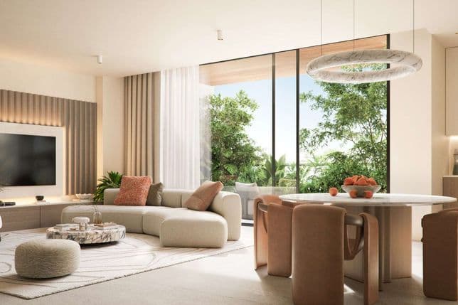 Elegant living and dining area with floor-to-ceiling windows, curved cream sofa, round marble table, and views of lush greenery blending indoor and outdoor spaces.