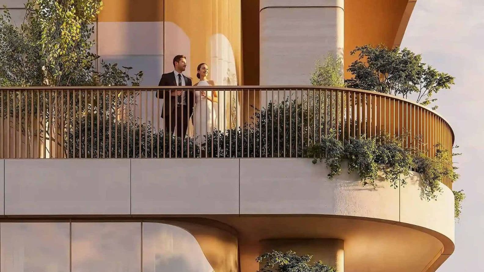 A couple stands on a modern balcony surrounded by lush greenery, set against a warm-toned building facade with large glass windows.