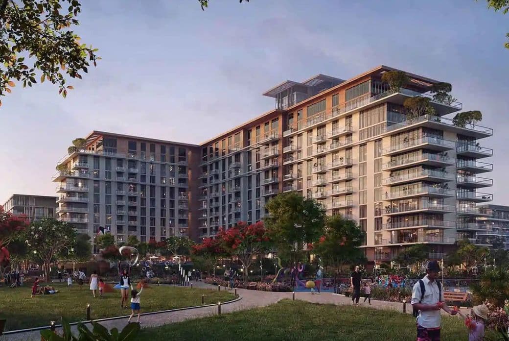 Modern apartment complex with balconies, surrounded by trees and a park. People are enjoying outdoor activities in the foreground.