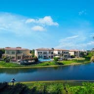 Luxurious lakeside villas with red-tiled roofs, surrounded by lush greenery under a clear blue sky, reflected in the tranquil water.