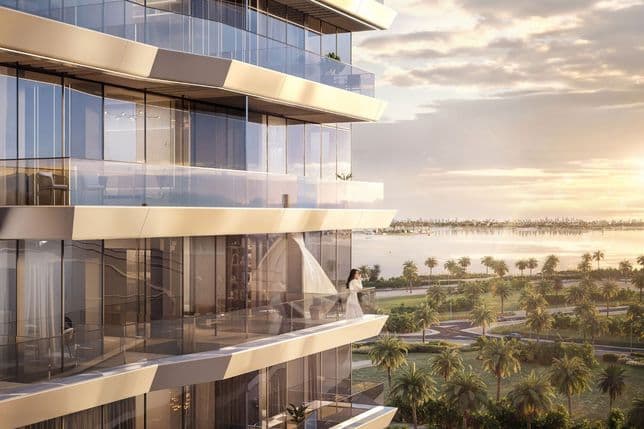 Modern high-rise building with glass balconies, overlooking a scenic view of palm trees and a body of water at sunset.