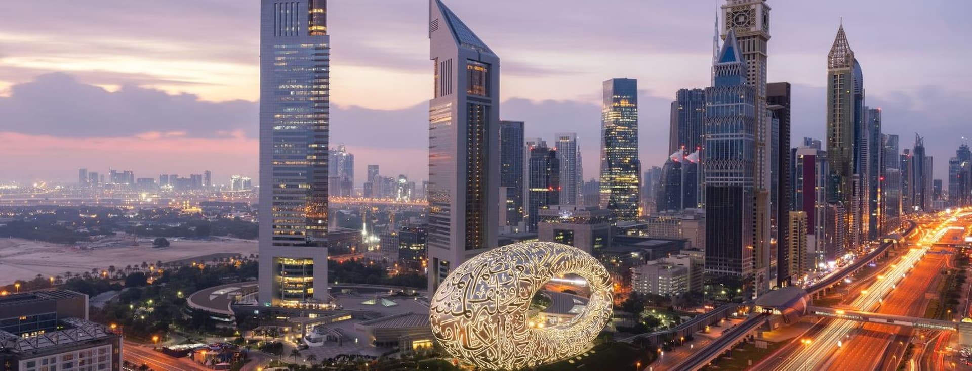 High-rise skyline of DIFC at sunset, with bright lights down Sheikh Zayed Road
