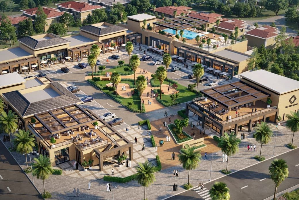 Aerial view of a modern shopping plaza with multiple buildings, outdoor seating, and landscaped areas surrounded by trees and roads.